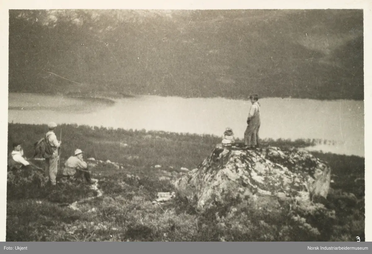 Over fjellet til Tomevatn på Møsstrond. To gutter står i fjellet ved en liten varde. Til venstre sitter og står tre menn iført turklær med hver sin ryggsekk