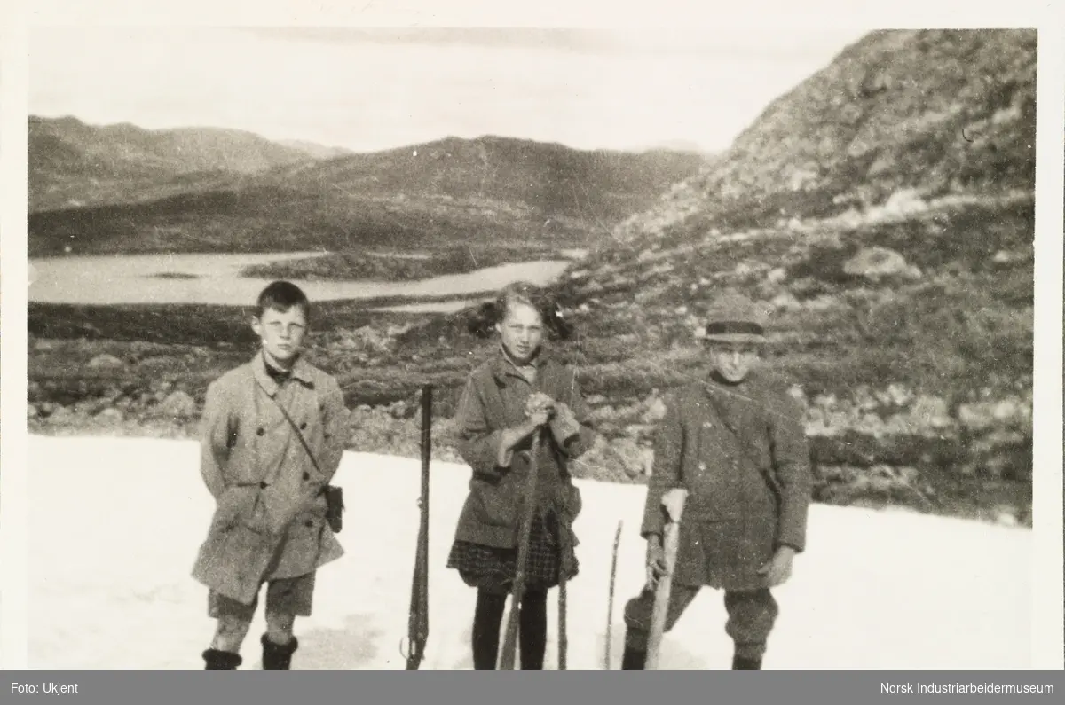 Møsstrond 1922. Jente og to gutter står på en snøflekk i fjellet på Møsstrond. De er iført turklær og har hvert sitt gevær. Antatt avbildet: Per/Jens B.W. (Bache-Wiig?), Annar og Berit.