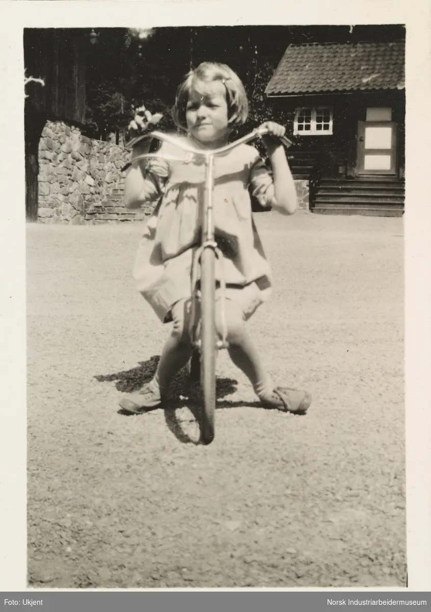 Sommeren 1931, Gullia og Fagerli. Jente i kjole sitter på sykkel på gårdsplassen på Gullia, Lysaker 1931.