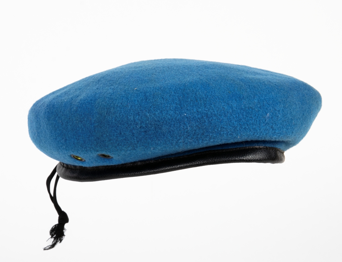 Blå basker med svart foder och svart läderkant. Märkt på insidan med (storlek) 7 1/4 och Kangol Wear Limited.