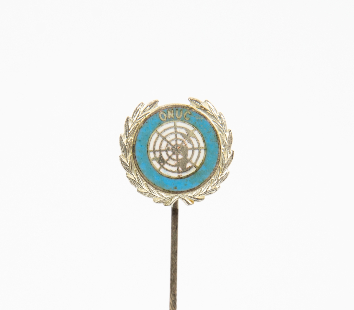 Kavajnål. Märke av metall med guldfärgat FN-emblem på vit botten och texten ONUC.