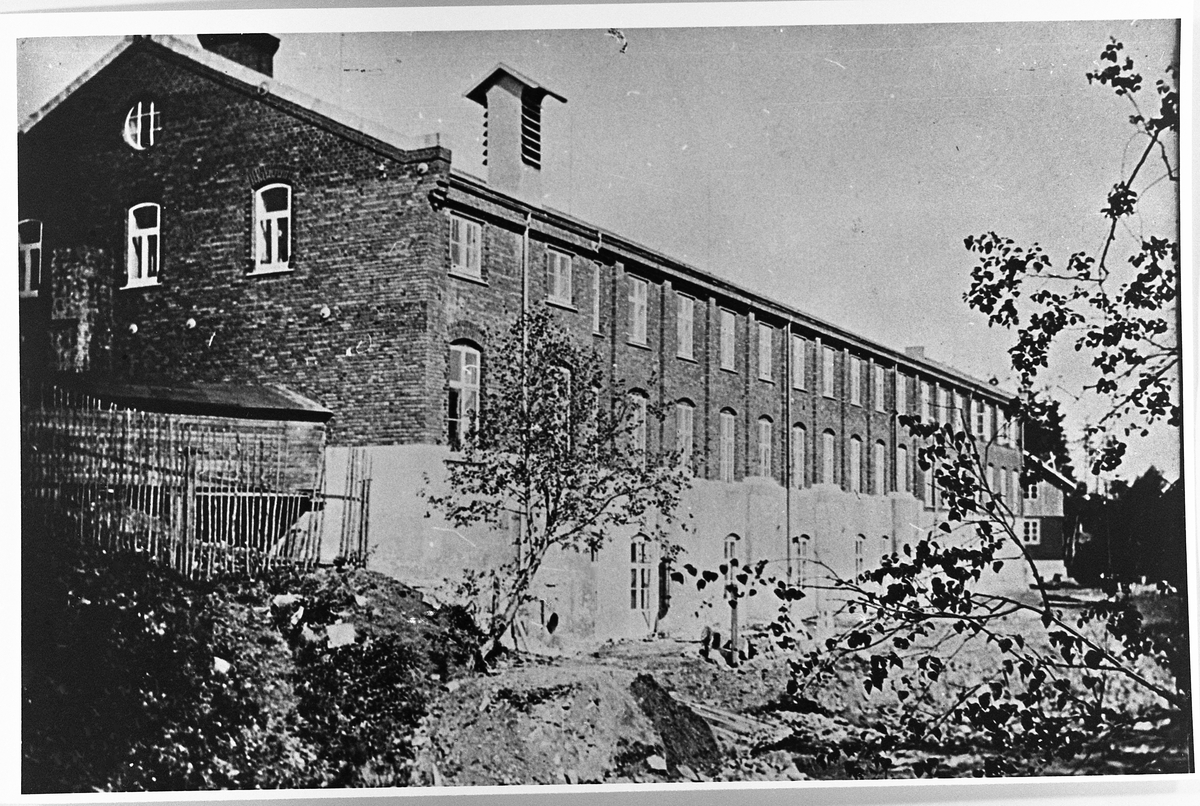 Raufoss Patronfabrikk ca. 1912. Bildet viser den gamle fabrikkbygningen, den tidligere fyrstikkfabrikken. Den lyse halvparten nederst er murer fra fyrstikkfabrikken. På grunn av tre branner var murene lenger opp i dårlig forfatning, og måtte tas ned og mures opp igjen, nå med murstein. Før var det gråstein.