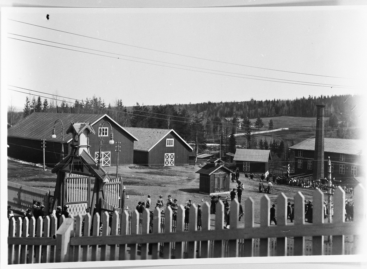 Raufoss Patronfabrikk ca. 1910. Bildet viser fabrikkporten med klokke i tårnet, og fabrikkplassen. To materialmagasin, og et lite brannhus midt på bildet. Den gamle fabrikkbygningen til høgre. På den andre sida av elva ser vi litt av Furuly og jorda som hørte til.