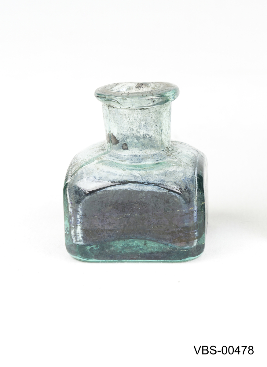 Firkantet flaske med avkuttede hjørner. 
Blekkhuset er støpt av blågrønt glass.