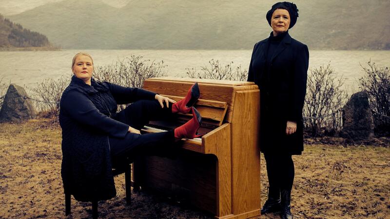 Inger Kristine Riber og Reidun Horvei poserer ved utendørs piano ved fjorden