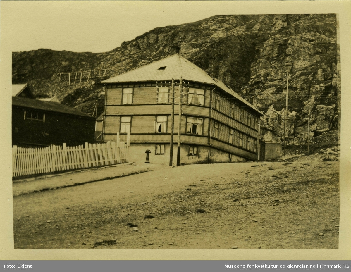 Hammerfest gamlehjem er i 1924 et vakkert trebygg med skifertak som står foran en fjellside med skredsikring. En strømmast og en brannhydrant står foran huset. Til høyre ligger et andre hus med gjerdet rundt.