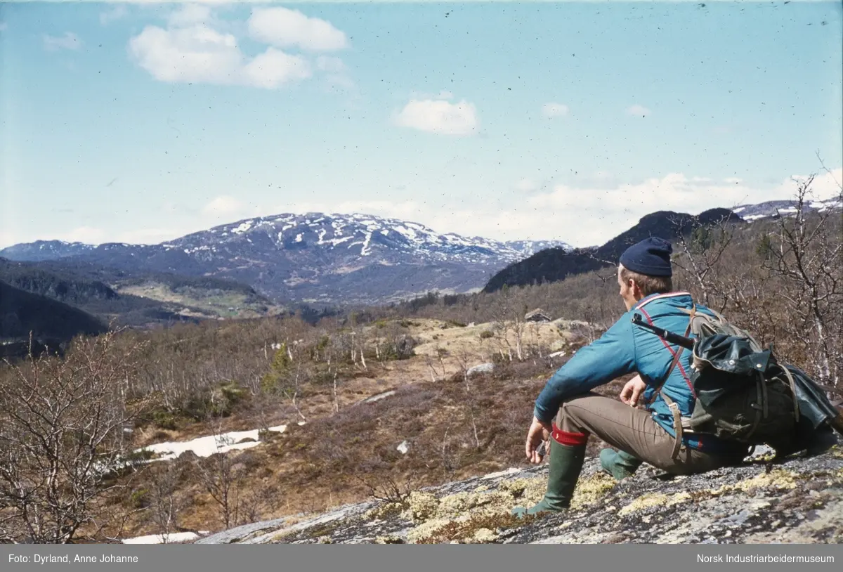 Bjørn Dyrland på jakt i Åmotsdal. Sitter å ser på utsikten mot Skuldalen med gevær og ryggsekk på ryggen