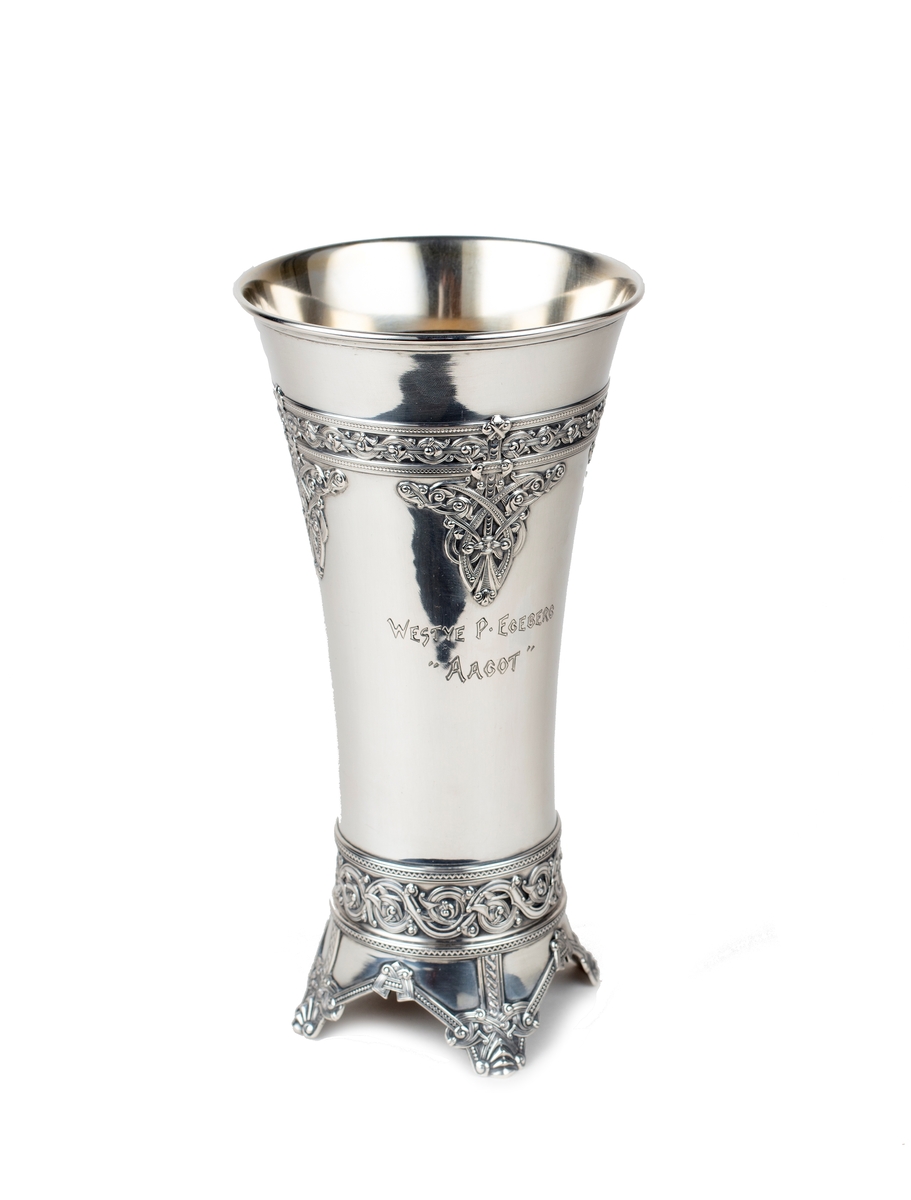 Pokal, sølv. Form som et middelalderbeger, dragestilsornamentikk. Stemplet på utsiden av et av bena.