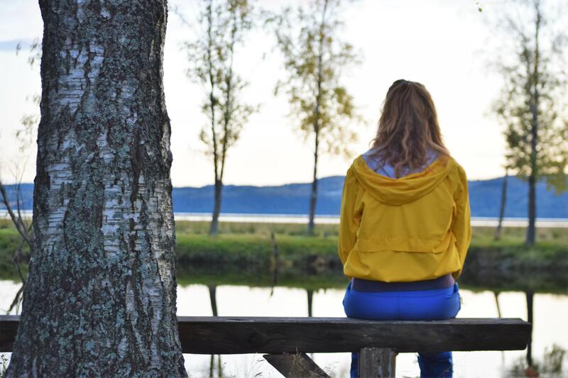 Foto av en jente som sitter på en benk og ser ut over Glomma