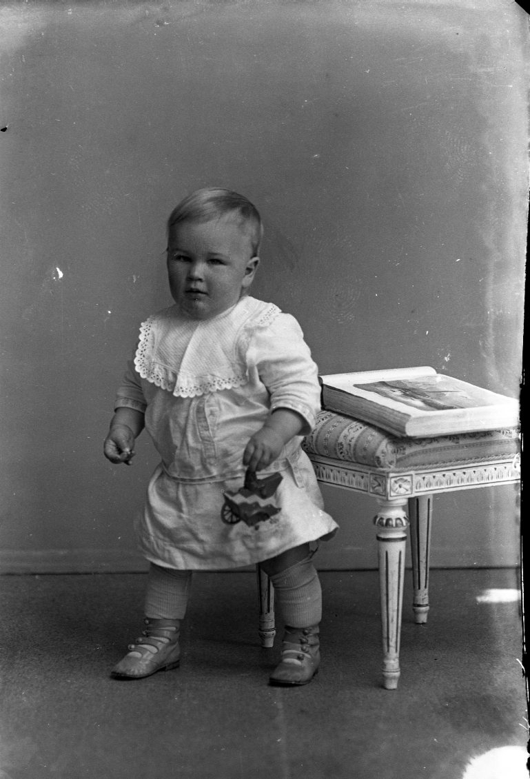 Porträtt av ett spädbarn - en liten pojk - som står mot en pall av gustaviansk stil.