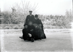 En mann og en kvinne står bak tre jenter som sitter på kjelk