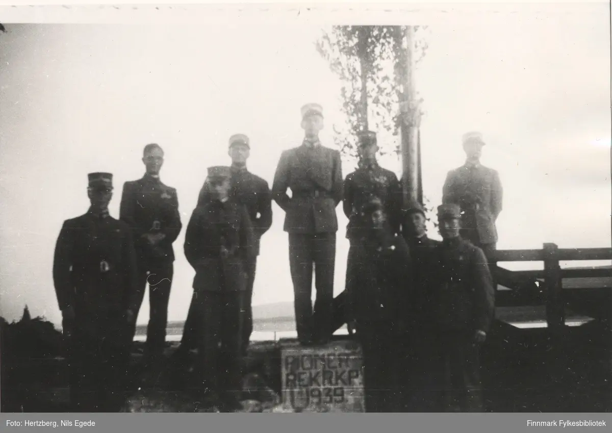 Ti militære menn ved bruen over Tanaelva i Seida. De har vært med på å bygge bruen og nå er den ferdig. "PIONER REKRKP. 1939" tekst på grunnmuren.