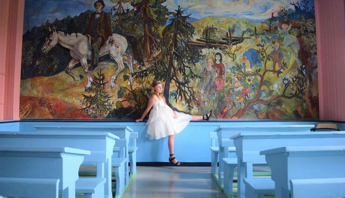 Jente i hvit kjole som står foran fargerikt veggmaleri på Stein skole (Foto/Photo)