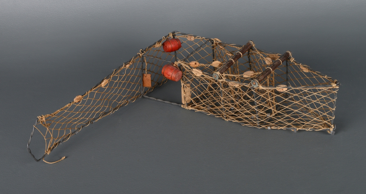 En modell av en kilenot med metallskjelett og nett. Laget av ståltråd, hyssing og kork. Den er montert og skrudd og tvinnet sammen. Viser hvordan redskapet fungerer for å fange laks.
