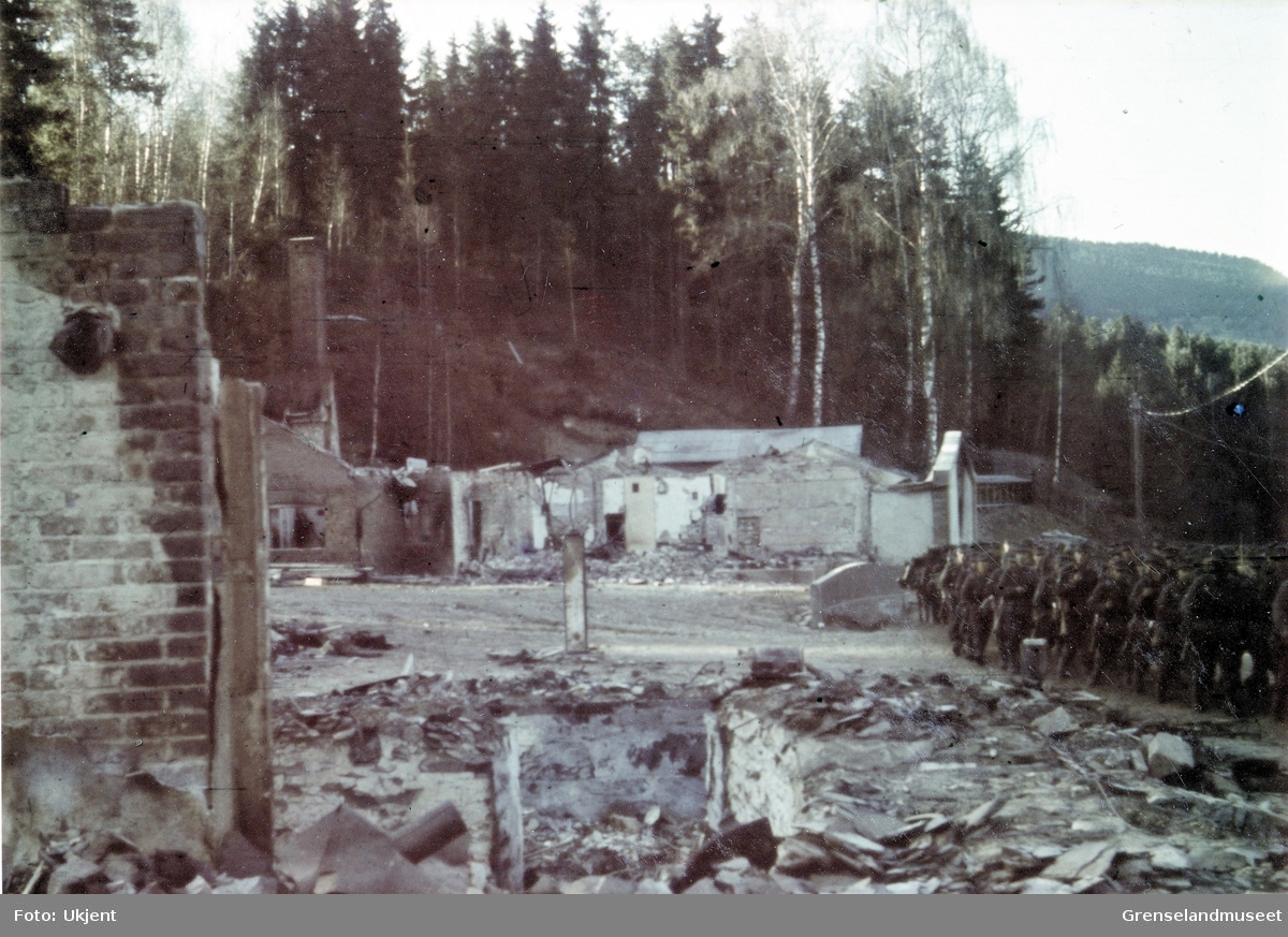 Soldater marsjerer forbi ruinen av et hus i en skog. 