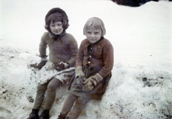 To unge jenter sitter på en snøkant i et snødekt landskap.