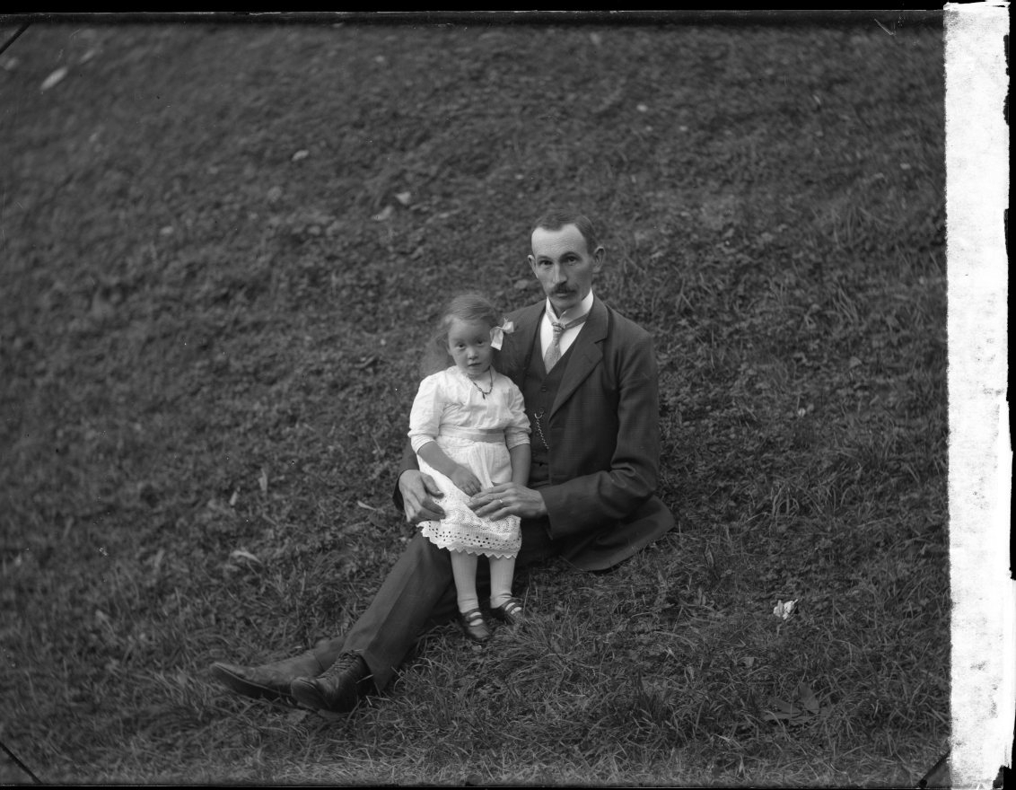 En man sitter i en grässlänt med en liten flicka i sitt knä. Flickan heter Astrid Almqvist, från Visingsö.