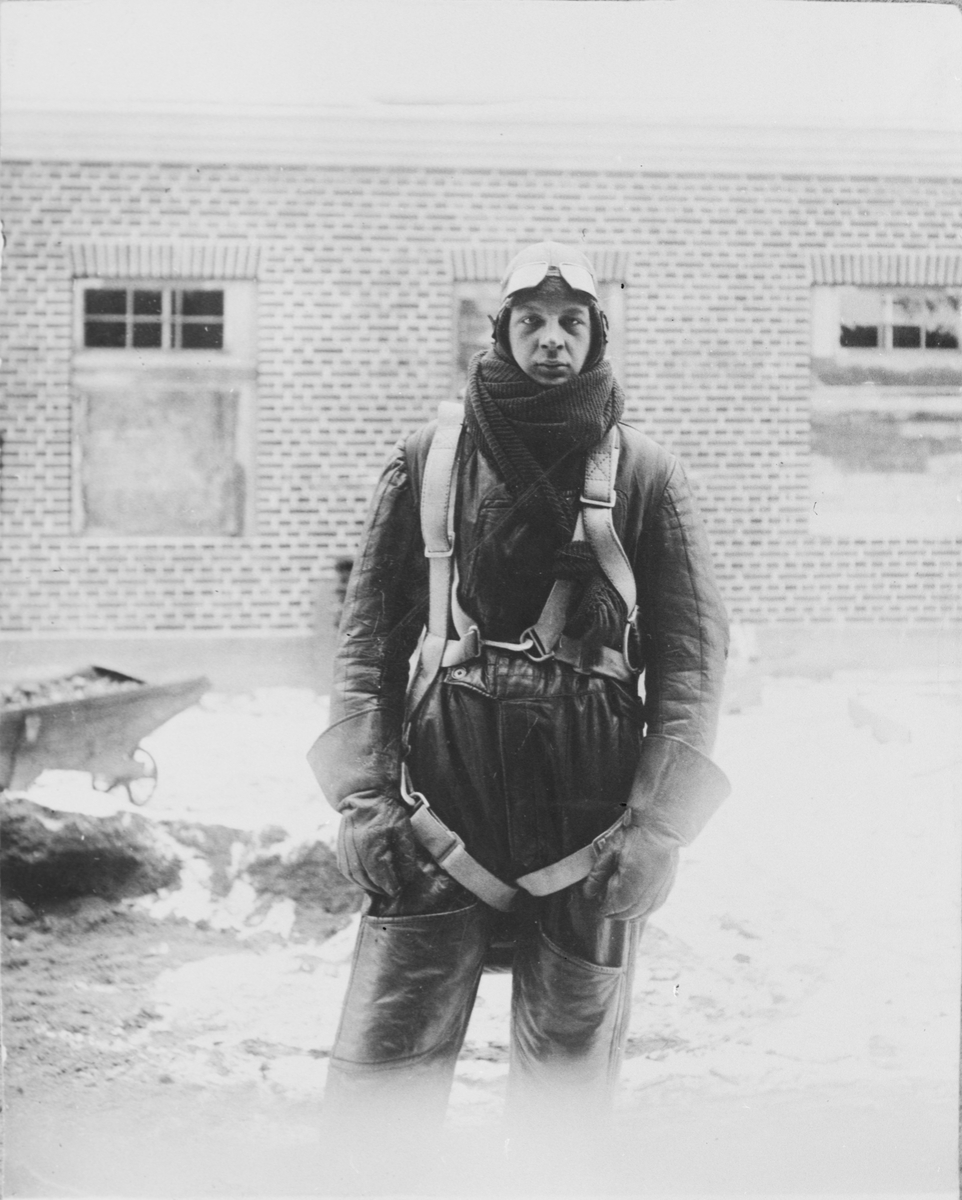 En man iklädd flygardräkt står framför en byggnad, ca 1920-tal.
