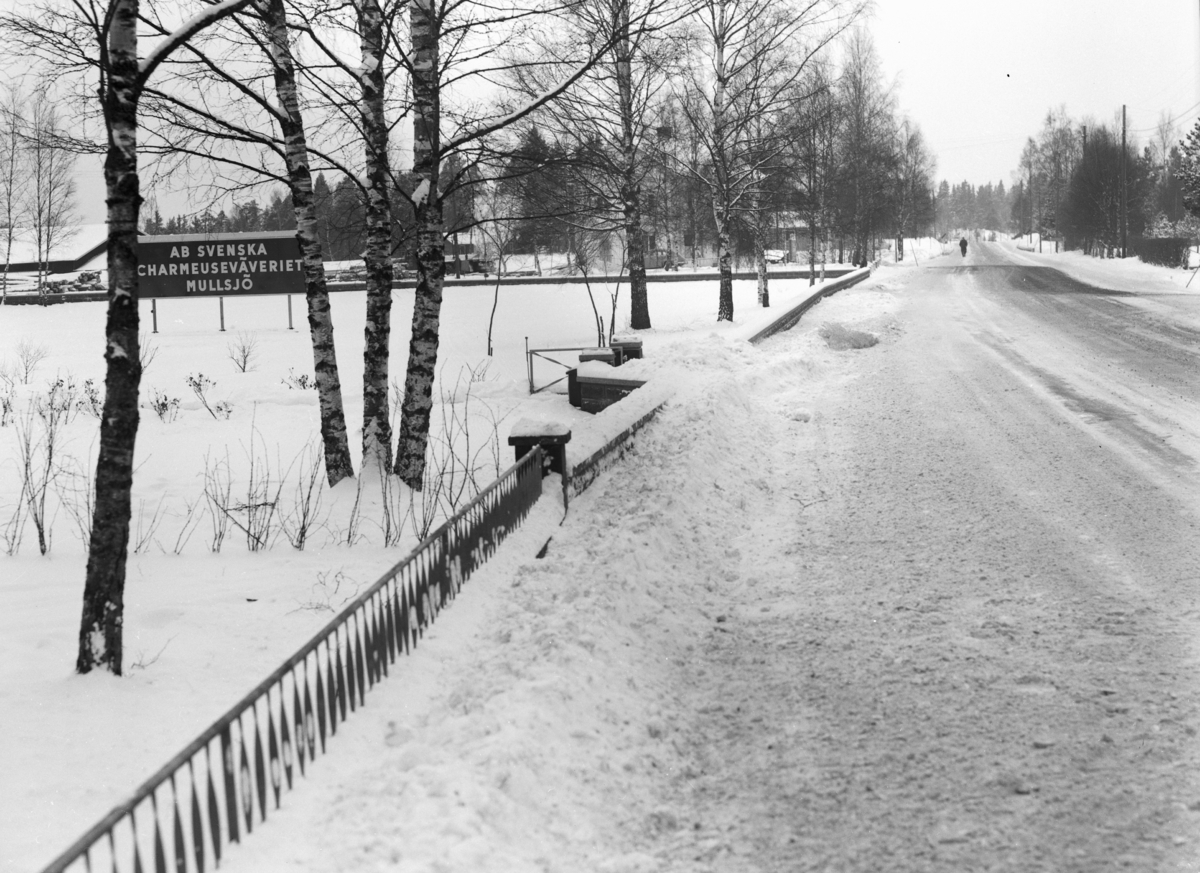 Vid en väg i Mullsjö står en skylt med texten, AB Svenska Charmeuseväveriet Mullsjö.