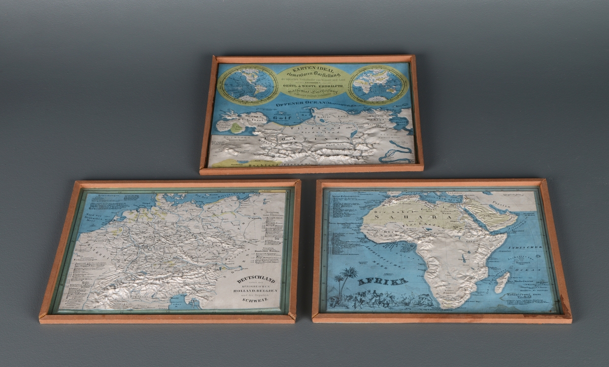 Syv rektangulære topografiske kart. Kartene er preget med reliefftrykk slik at topografien er opphøyet. Det er et kart over Sør-Amerika, et over Nord- og Mellom-Amerika, et over Afrika, et over Asia, et over Australia og Polynesia, et over Nederland og et over Tyskland. Kartene er innrammet i tre, og på kartet over Sør-Amerika er rammen ødelagt på toppen. Kartene over Sør- og Nord-Amerika er stående, og de andre er liggende. Alle kartene er skrevet på tysk.