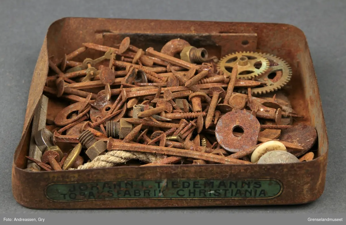 Tobakkseske i metall fyllt med sm[ spiker, stifter, tannhjul, muttere, knapper og skruer. Alt rustet.