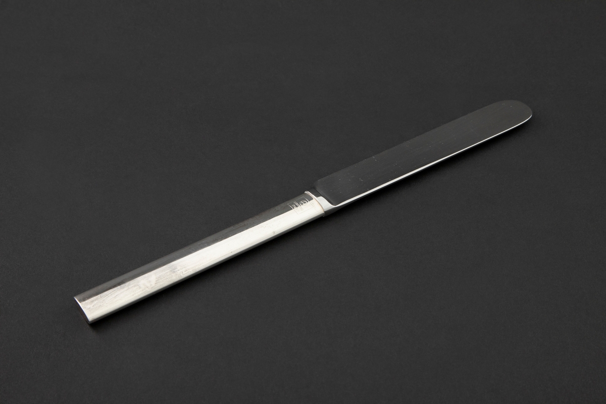 Stor kniv i sølvplett. Ovalt skaft med rett avslutning og bredere knivblad. Fra bladets halvrunde avslutning er egg og rygg parallelt.