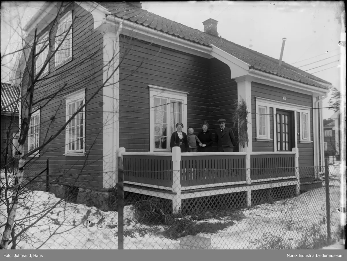 Hus med fire personer stående på terrassen. To kvinner, en mann, og et barn.