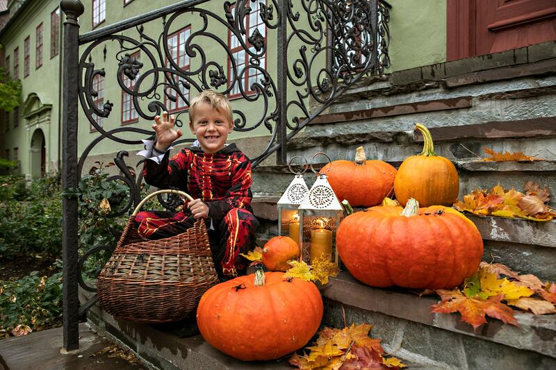 Gutt i halloween-kostyme sitter på en trapp med gresskar rundt