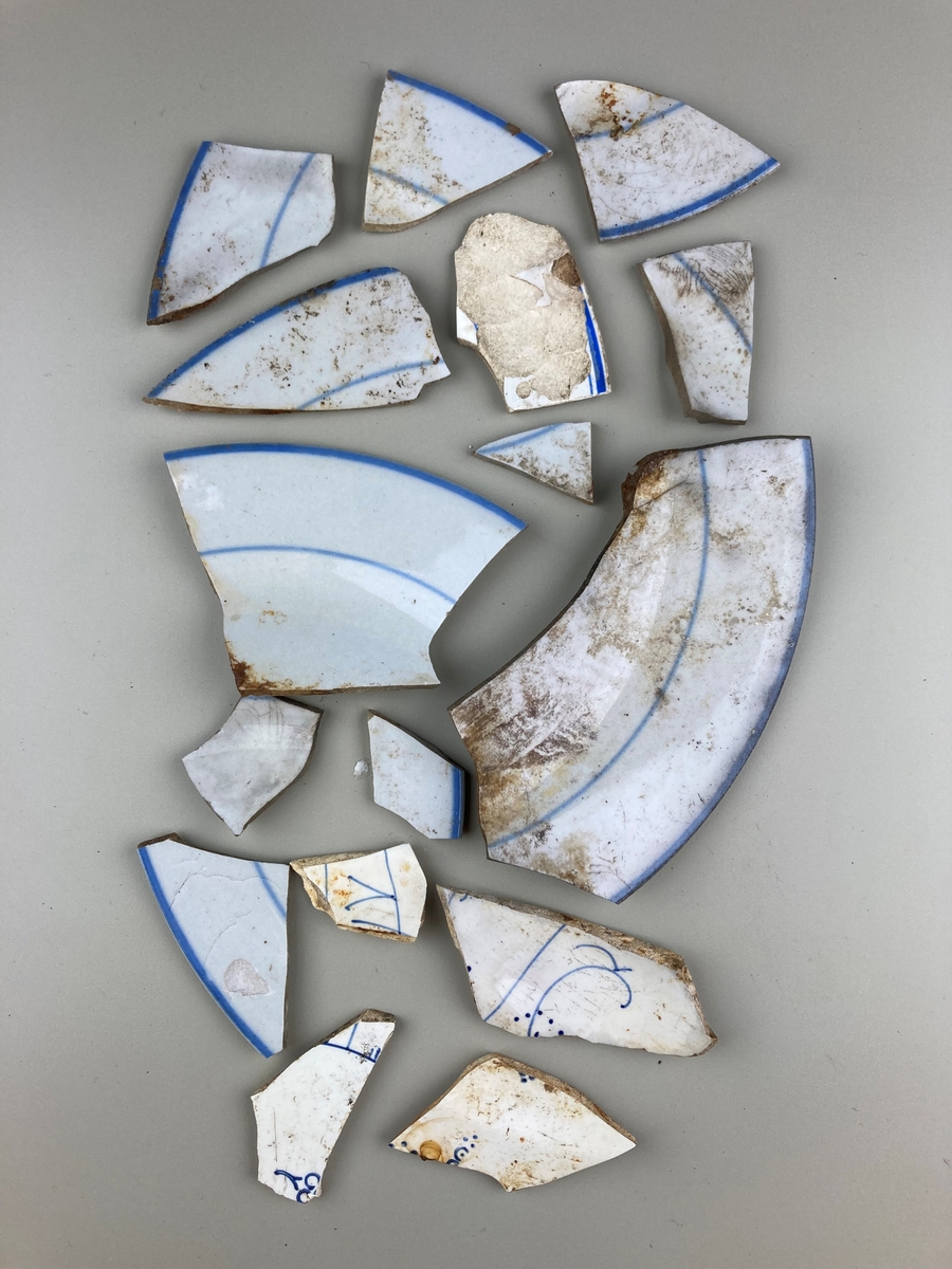 14 mindre fragment og to større fragment av porselen med blått mønster.