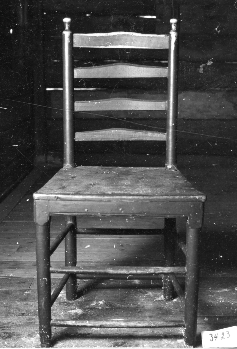 Brunmålad stol med raka svarvade ben och dubbla tvärslåer mellan benen, påpinnad sits. Genombruten rygg med svarvade stolpar och avslutade knoppar, mellan dessa 4 tvärslåar därav s.k. stegstol.
Likadan som inventarienummer 3424