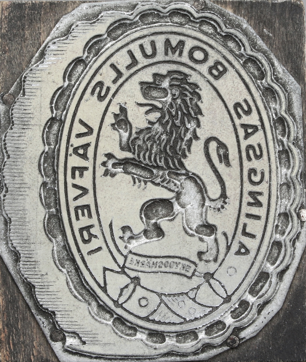 Kliché i vitmetall, limmad på rektangulär träplatta. Motiv i form av oval medaljong, med "stegrande lejon" och texten
"ALINGSÅS BOMULLS VÄEVERI". Ytterst vågmönstrad uddbård. Proveniens Alingsås Bomullsväveri AB, Alingsås.

Alingsås Bomullsväveri lades ner 1970.

Alingsås bomullsväveri AB grundades 1862 i Alingsås.

Väveriet startades av Charles Hill och samtidigt invigdes Västra stambanan, vilka tillsammans fick enorm betydelse för Alingsås utveckling.

Firman ombildades 1884 till aktiebolag och uppköptes 1912 av Nääs fabriksaktiebolag. Den bestod av ett bomullsväveri, ett blekeri, färgeri och appreturverk. År 1946 hade firman omkring 550 anställda, vilka producerade oblekta, blekta, färgade och kulörta bomullsvävnader. Det var stadens dominerande arbetsgivare, och tack vare att även besläktad verksamhet etablerades förknippades Alingsås starkt med textilindustrin. 

Fabriksbyggnaderna i centrala Alingsås revs i mitten av 1960-talet. (Wikipedia)