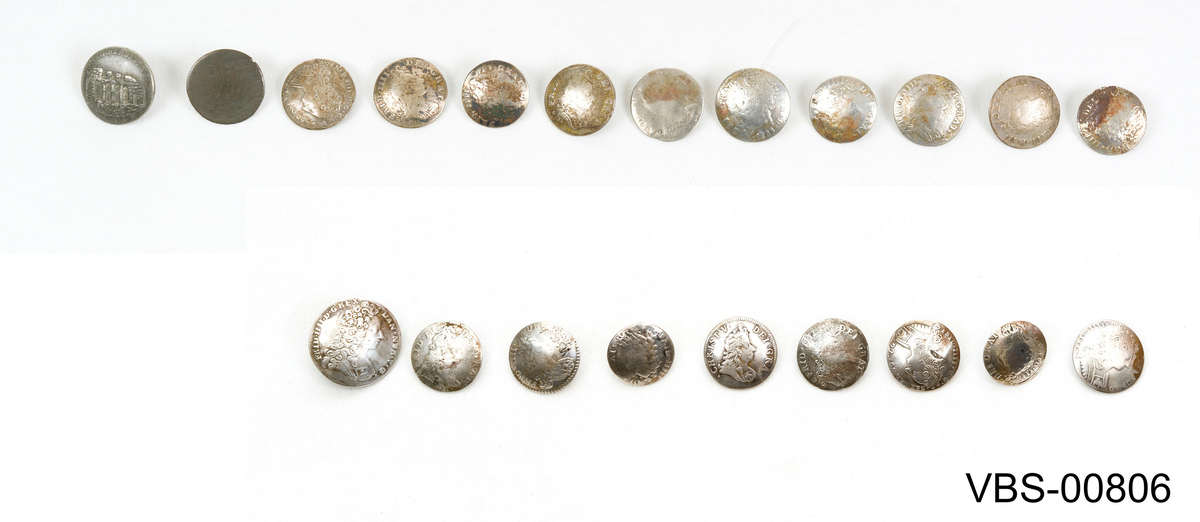 Samling av 21 sølvknapper, i forskjellige størrelser som er omlagd av shilling mynter.
Avrundete i form, i det indre konvekse området, har de en liten sveiset ring å sy til plagget
