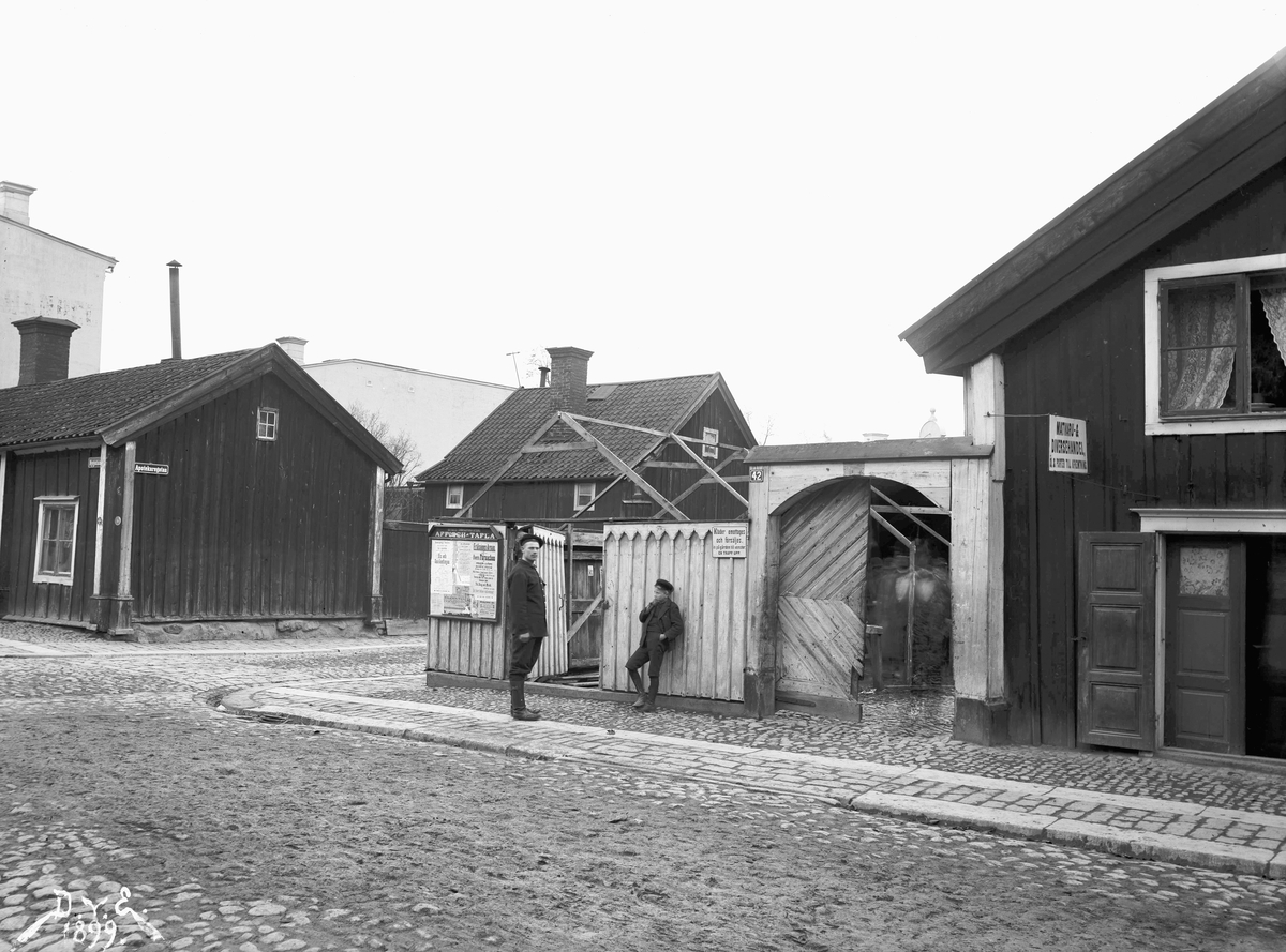 Parti av Linköping år 1899, närmare bestämt Nygatan 42 vid skärning med Apotekaregatan. Byggnaderna illustrerar den enklare trähusbebyggelsen som länge dominerade stadsbilden. Brandgavlarna som skymtar i bakgrunden visar ändå på den nya tiden där stora stadsmässiga bostadshus börjar förändra stadsbilden.