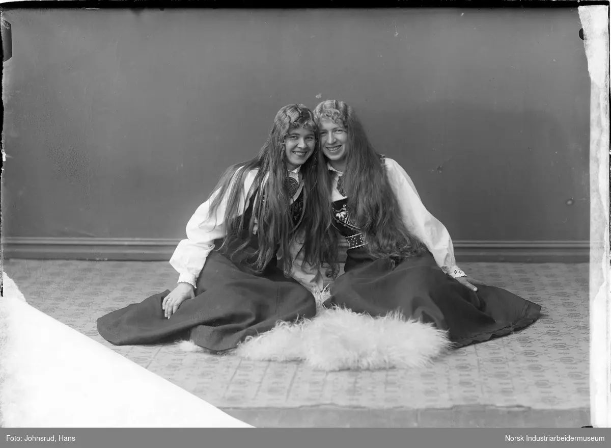 Portrett av to kvinner sittende i bunad på en pels
