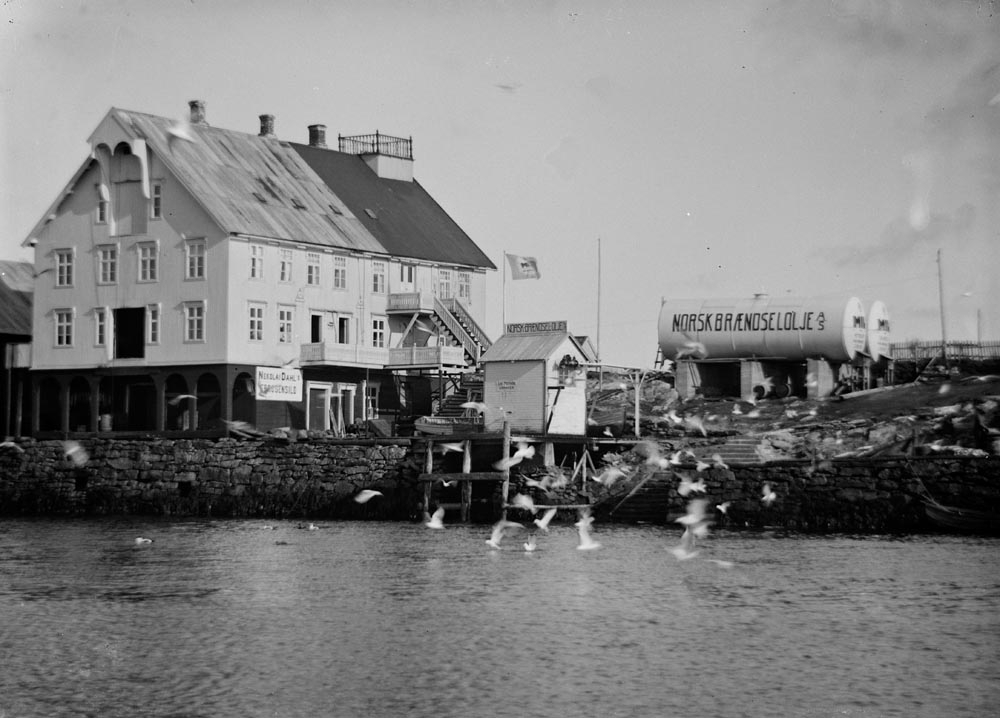 Røst. Kårøya og Helgesenhuset, legg merke til utkikksposten/altanen på taket av huset. På skiltet på veggen står det: Nikolai Dahl. Det var her fiskeflåten fikk fylt drivstoff, antatt levert av Norsk Brændselolje as.