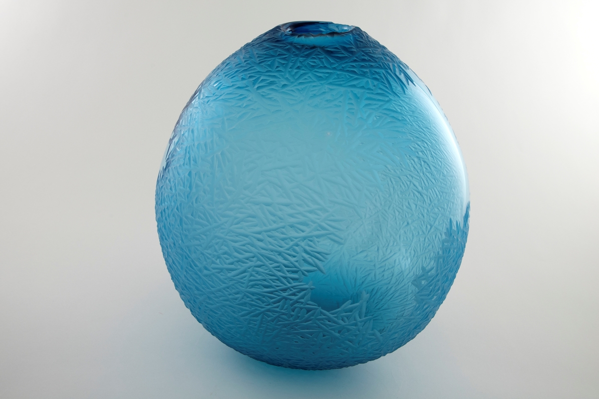 Asymmetrisk dråpeformet skulptur i blåfarget klart glass. Deler av overflaten er behandlet med sliping, sandblåsing og polering, slik at det oppstår en matt struktur av kryssende diagonale linjer som skaper assosiasjoner til rim/frost. Slik dannes det en virkningsfull kontrast til de ubehandlede partiene, som muliggjør at betrakteren kan studere dekoren fra både ut- og innsiden. Sirkulær åpning ved vasens topp.