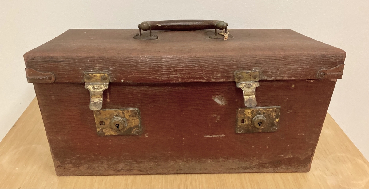 Brun liten koffert med håndtak og låsbar lukkemekanisme.