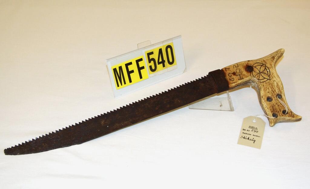"Sticksåg av järn, som skissen, med snidat och vinkelböjt handtag av renhorn med 4 hål på ena sidan inristat cirkelornament samt "H O S" och "1697". Framtill är handtaget bandat med en järnring. Längd 45 cm, därav handtaget 13 cm. Sågbladets bredd 3,3 cm. (skiss) - Ristat mönster i dekoren: ett blommotiv, karaktäristiskt för Nord-Lappland. Gåva av bokbindarmästare Alb. Hörnlund, Ängom." (Ur Lappkatalogen. Arvid Enqvist 1936)

