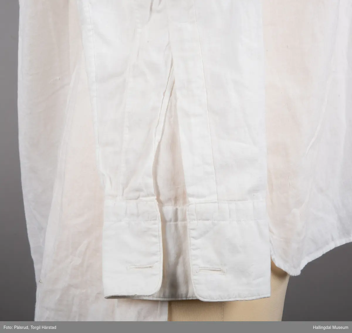 En hvit herreskjorte i bomull med folder på skjortebryst og to knapper. Uten krage i hals, med to knapphull i halslinningen og et knapphull bak. To knapphull i hver ermelinning til mansjettknapper. Splitt i sidene.