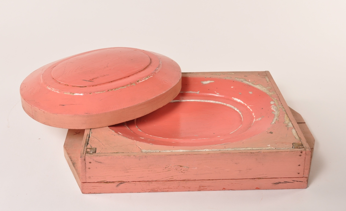 Modell av rosamalt og rødmalt tre i to deler til en grunn, oval fasong. Utydelig påskrift på den store delen [... ovn]