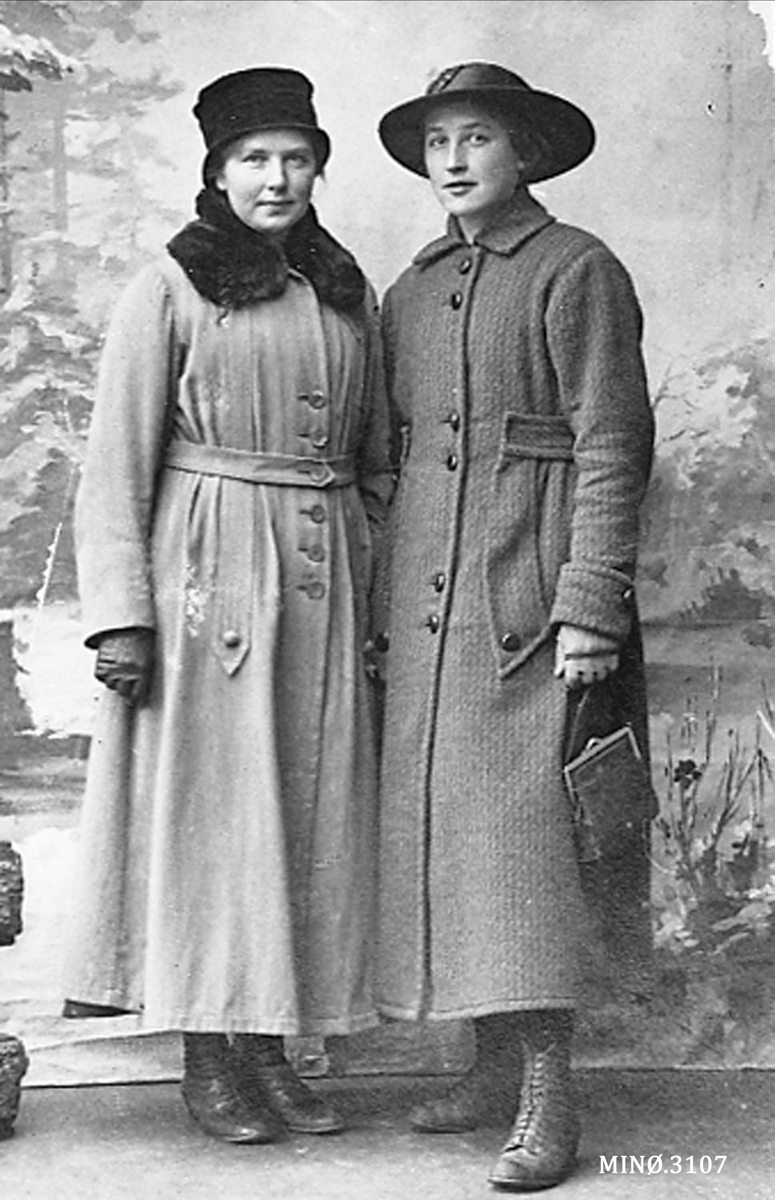 To damer oppstilt, med håndveske, kåpe og hatt. 