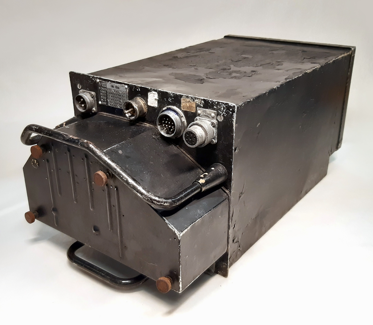 SM-enhet till flygradio FR 8. Bestående av en svart låda i metall, med i fronten ett utskjutande parti med fyra stick-kontakter, samt två bärhandtag.