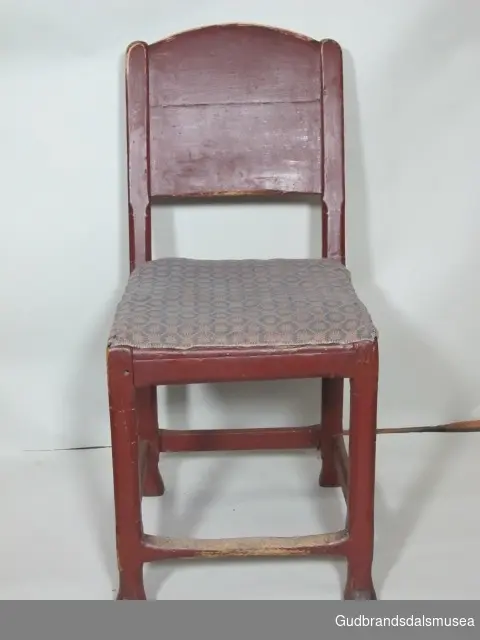 Enkel stil. Ryggens bakside er skåret i kraftig relieff. Setetrekket er stoppet og har ulltrekk. Trekket er mønstret i hvitt og blått. Stolen har ikke armlen.