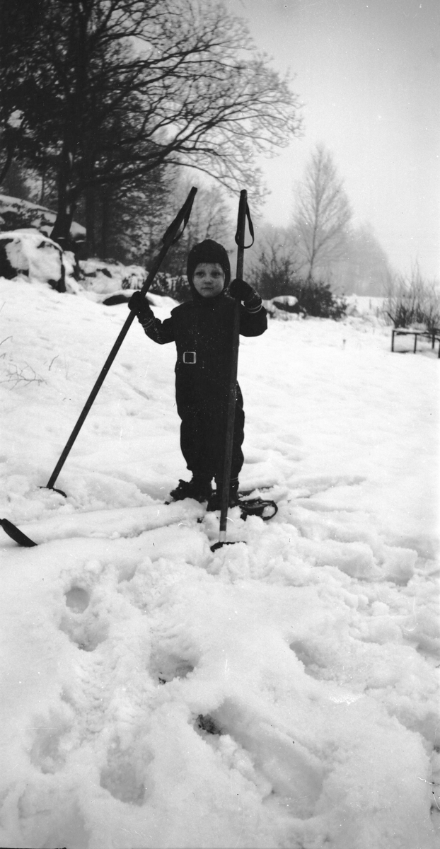Litet barn i overall på stora skidor och stavar.