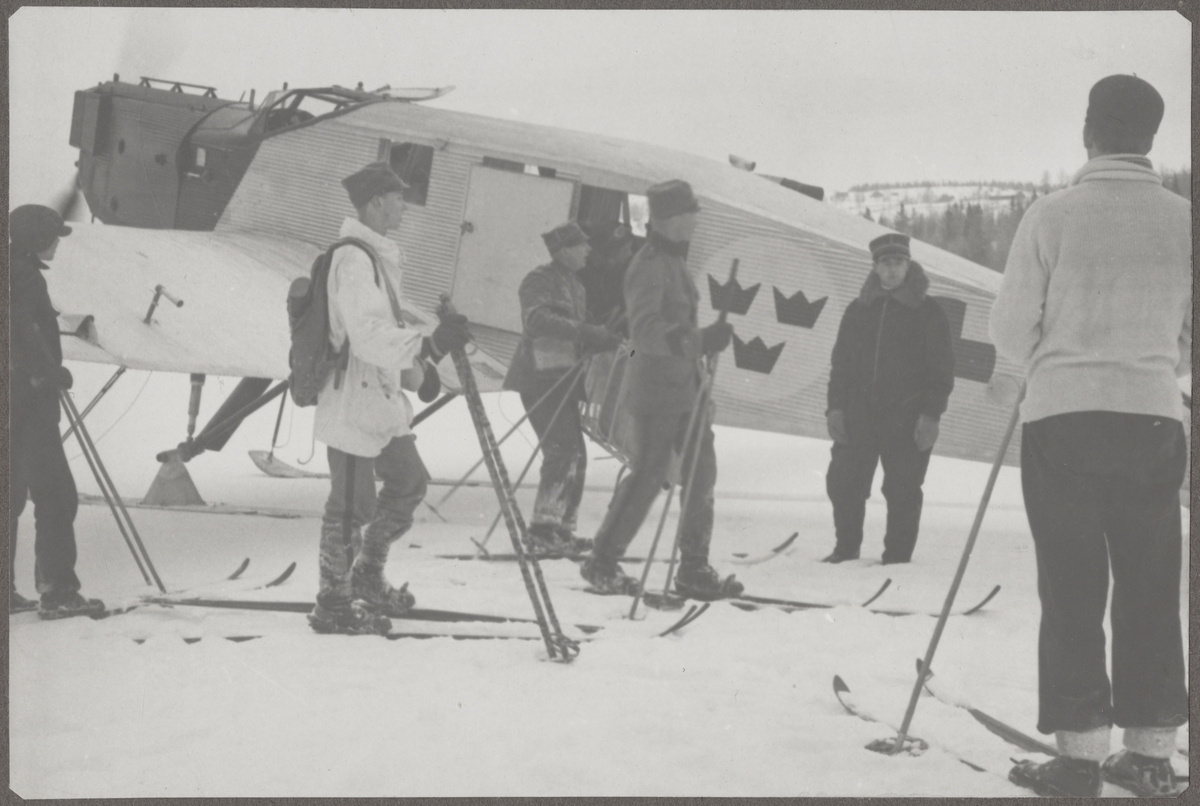 Militärer på skidor står vid ambulansflygplan Trp 2, Junkers W 34, vintertid. Flygare vid planet.