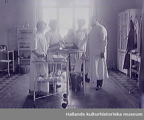 Läkare, tre sjuksystrar och flickpatient på operationssal. Man lägger om bandage om barnets fot. (Se även bild MR2_1000)