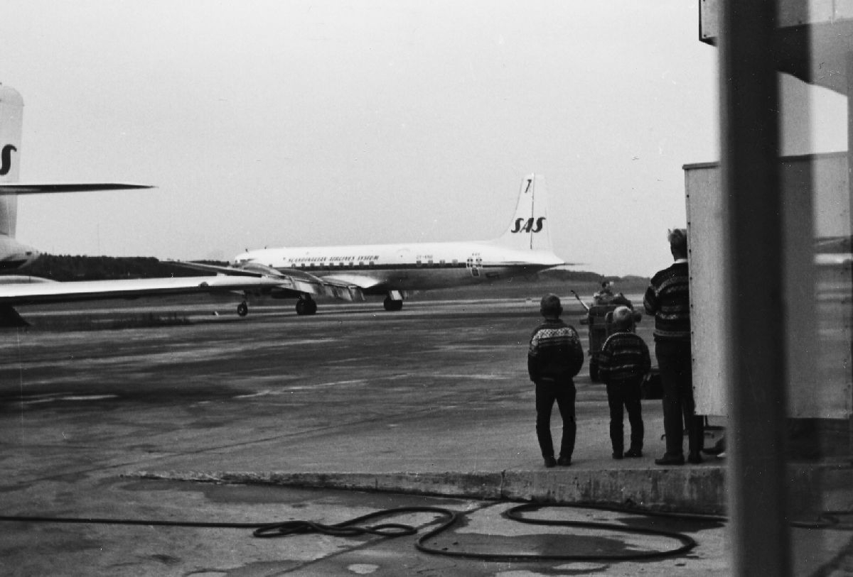 En DC-7C fra SAS taxer ut fra oppstillingsområdet på Bodø flyplass, mens to barn følger spent med.