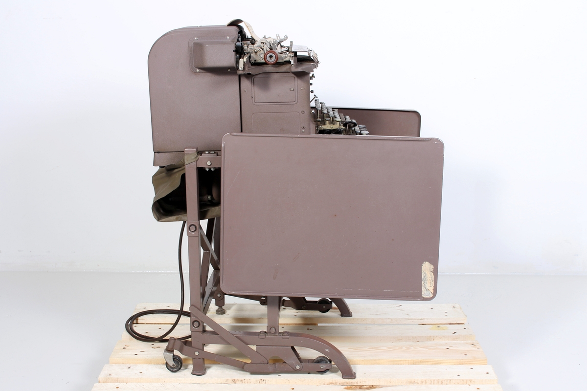 Kombinert regne- og skrivemaskin. Montert på stålrørsstativ med hjul og sammenleggbare bordplater. 
En uferdig faktura sitter igjen i maskinen - denne er datert 12. mars 1985 og avsender er merket Øglænd Metallgruppen.