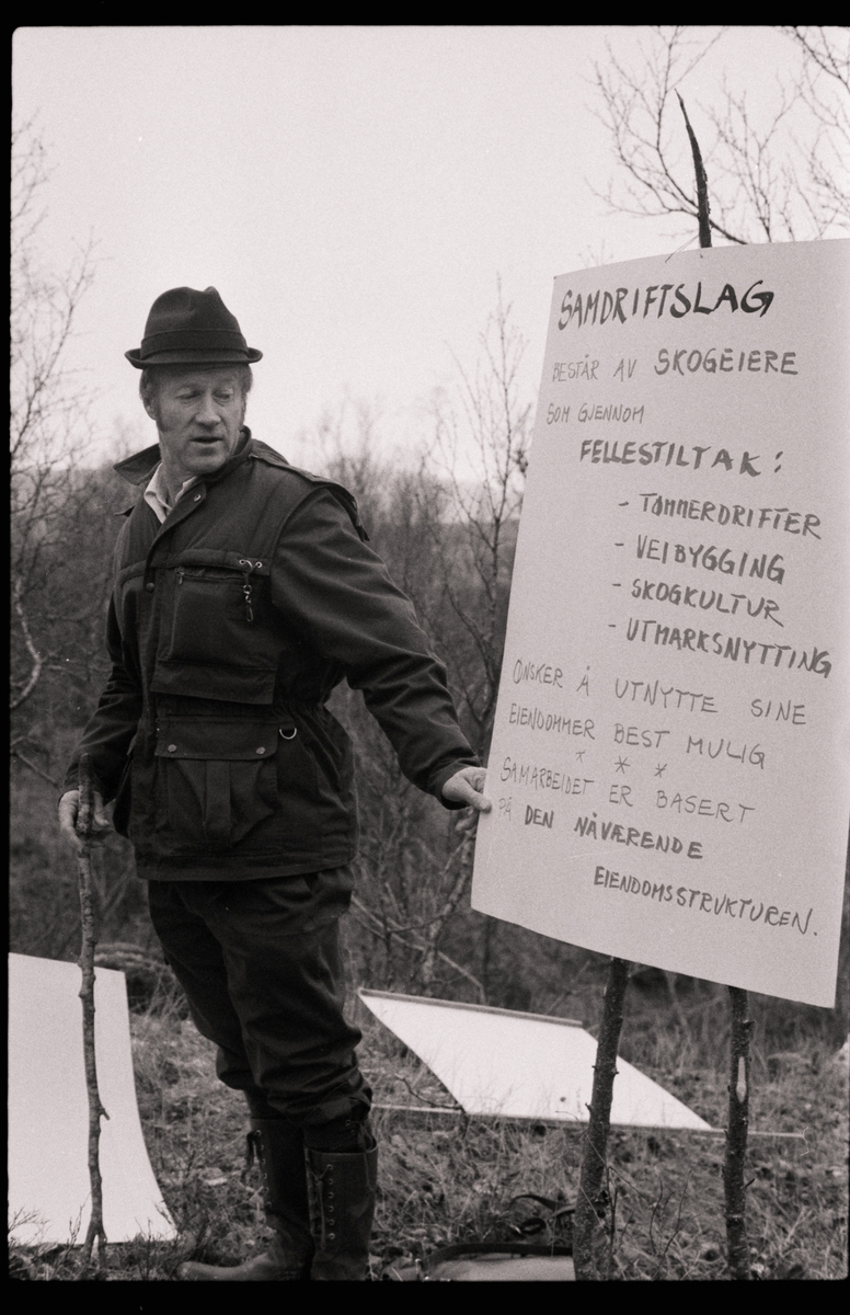 Mann viser frem plakat som forteller om formålet til et samdriftslag for skogeiere .