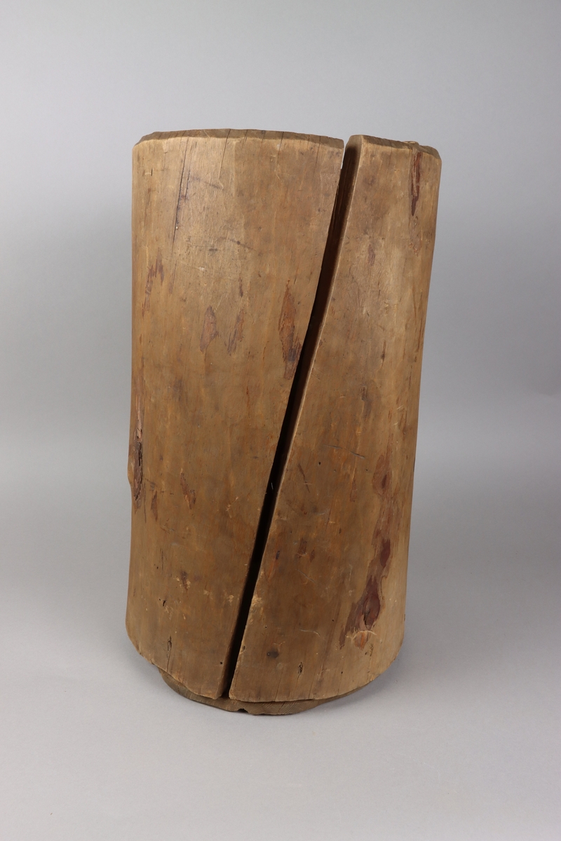 A wooden barrel, carved from the trunk of the tree, below a flat cylindrical end attached with dowels up on the sides of the vessel.
